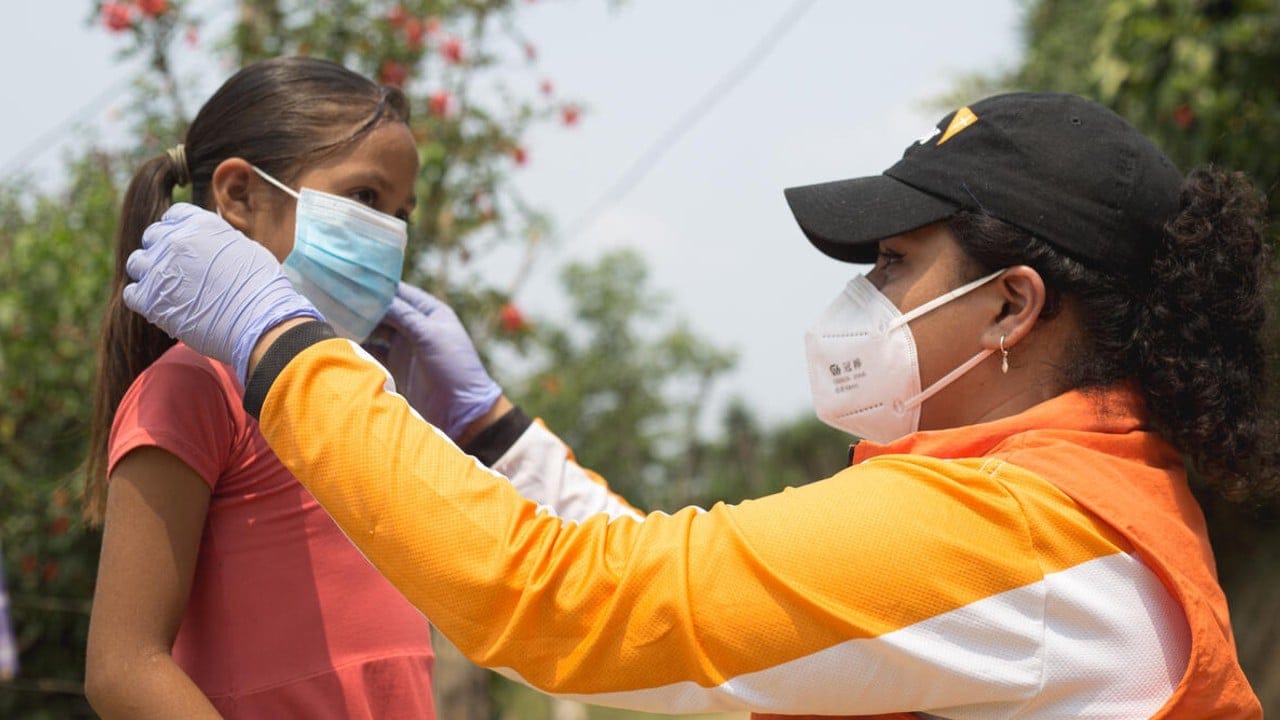 World Vision staff helps child put on a mask for COVID-19