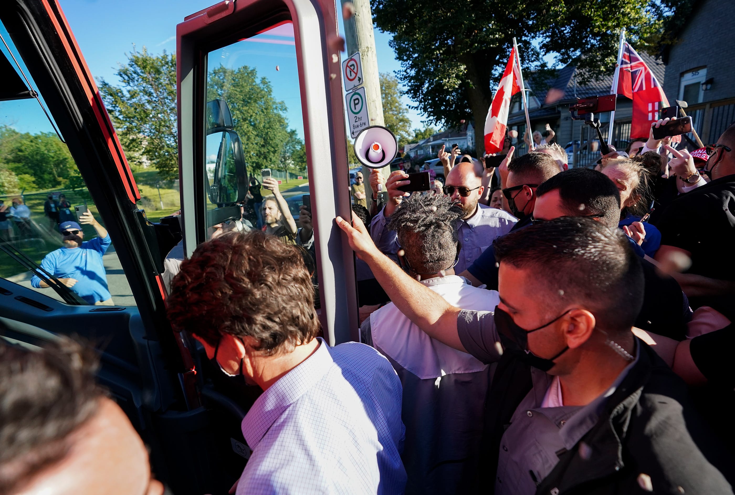 Gravel is thrown at Liberal leader Justin Trudeau, left, as the RCMP security detail provide protection, while protesters shout at a local microbrewery during the Canadian federal election campaign in London Ont., on Monday, September 6, 2021. (Nathan Denette/CP)