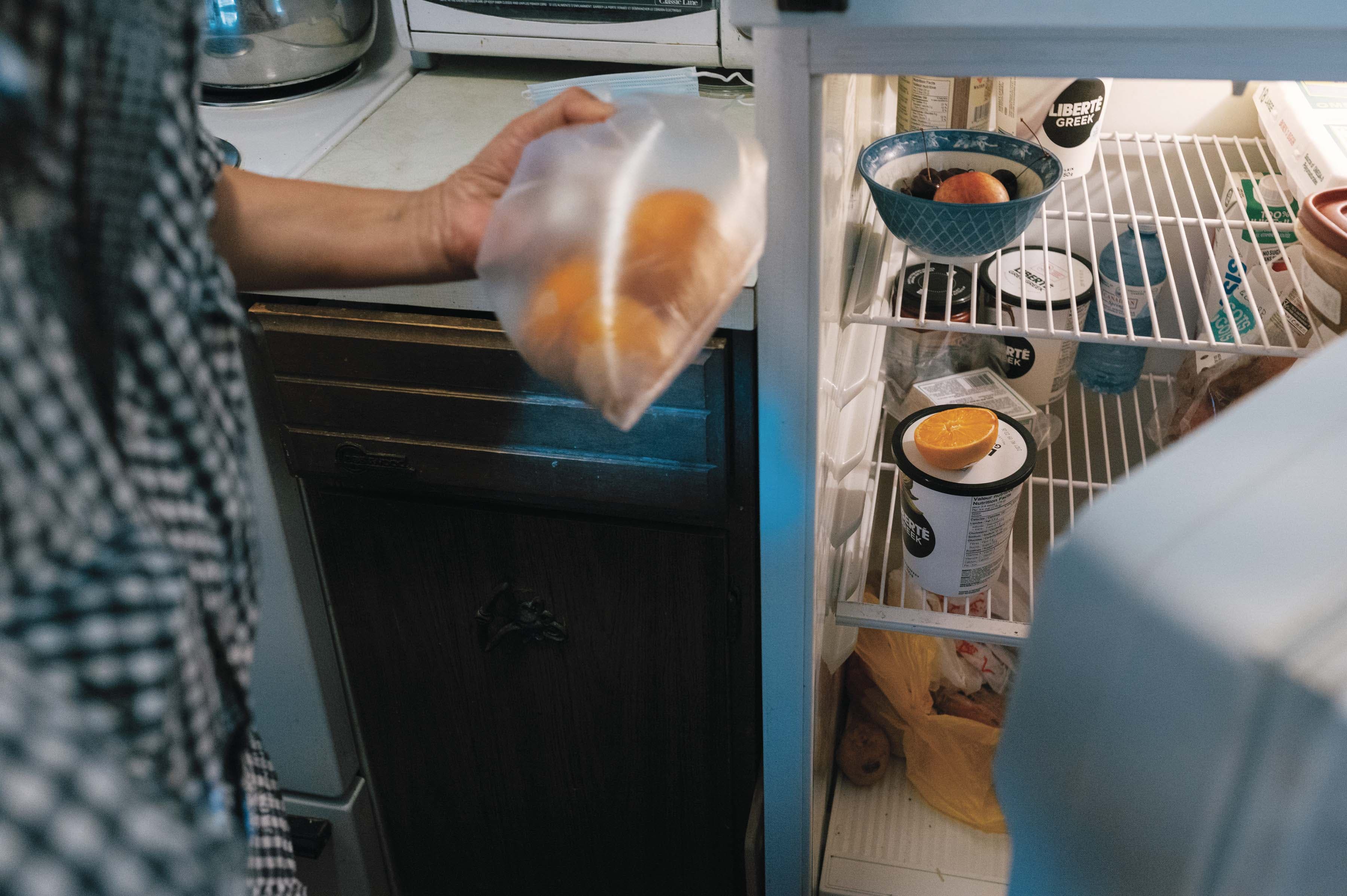 Xiao Wen Shi, 73 reaches into her fridge for a bag of oranges, one of the items included in the weekly delivery of a subsidized grocery program. (Photography by Felicia Chang)