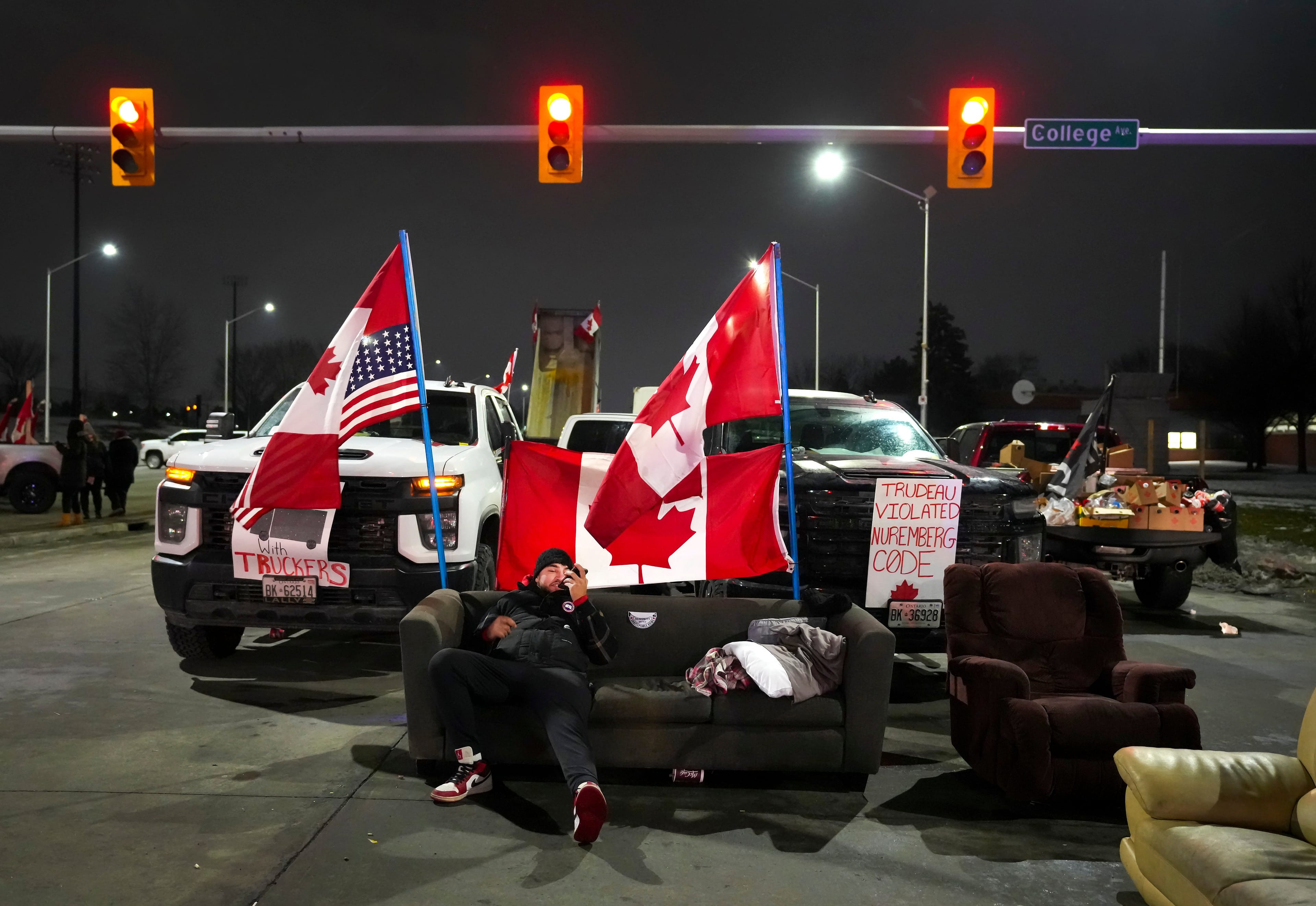 A trucker supporter sits on a couch as they block the access leading from the Ambassador Bridge, linking Detroit and Windsor, Windsor, Ont., February 9, 2022. (Nathan Denette/The Canadian Press)