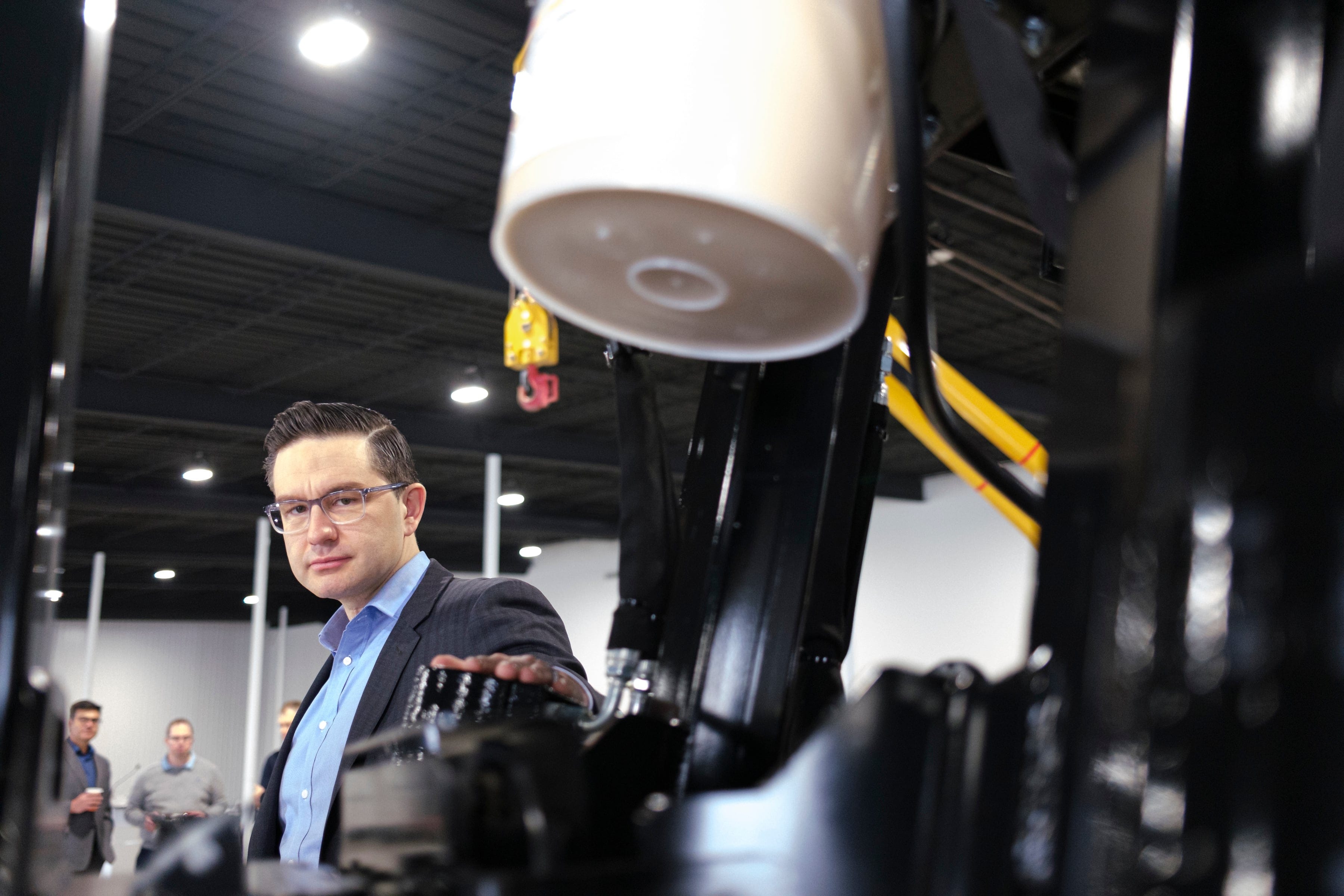 Poilievre glances at the camera briefly while getting a tour of machinery in Regina March 4, 2022. (Michael Bell/The Canadian Press)
