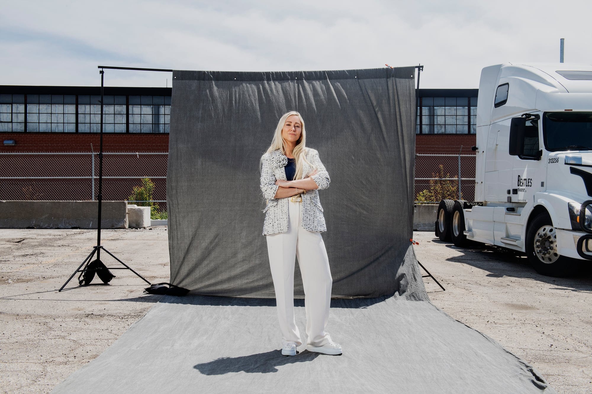 A blonde woman in a white pantsuit standing in front of a grey backdrop
