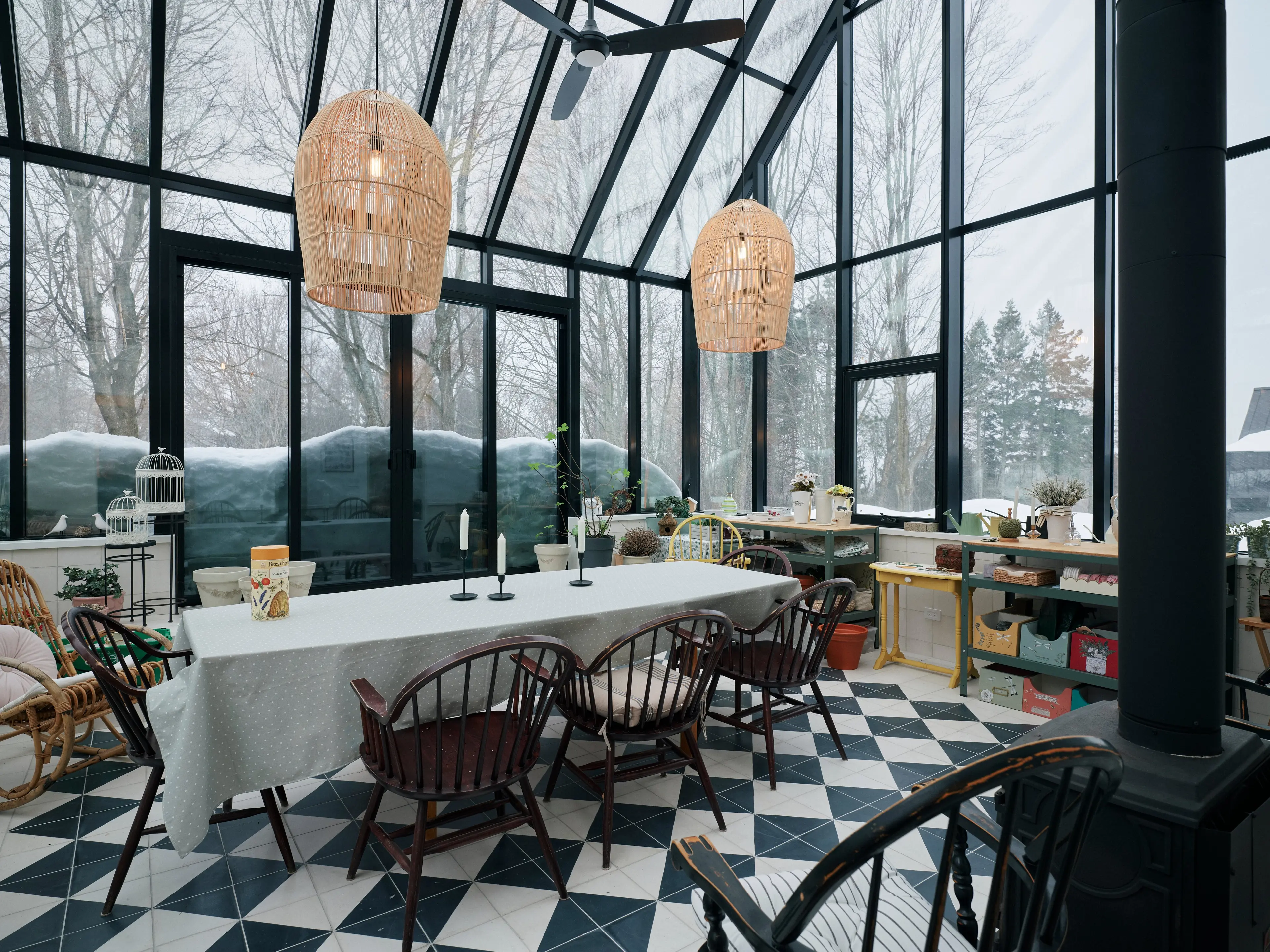 A solarium with high ceilings and a checkerboard tile floor. There are wicker pendant lights and craft supplies on shelves against one wall