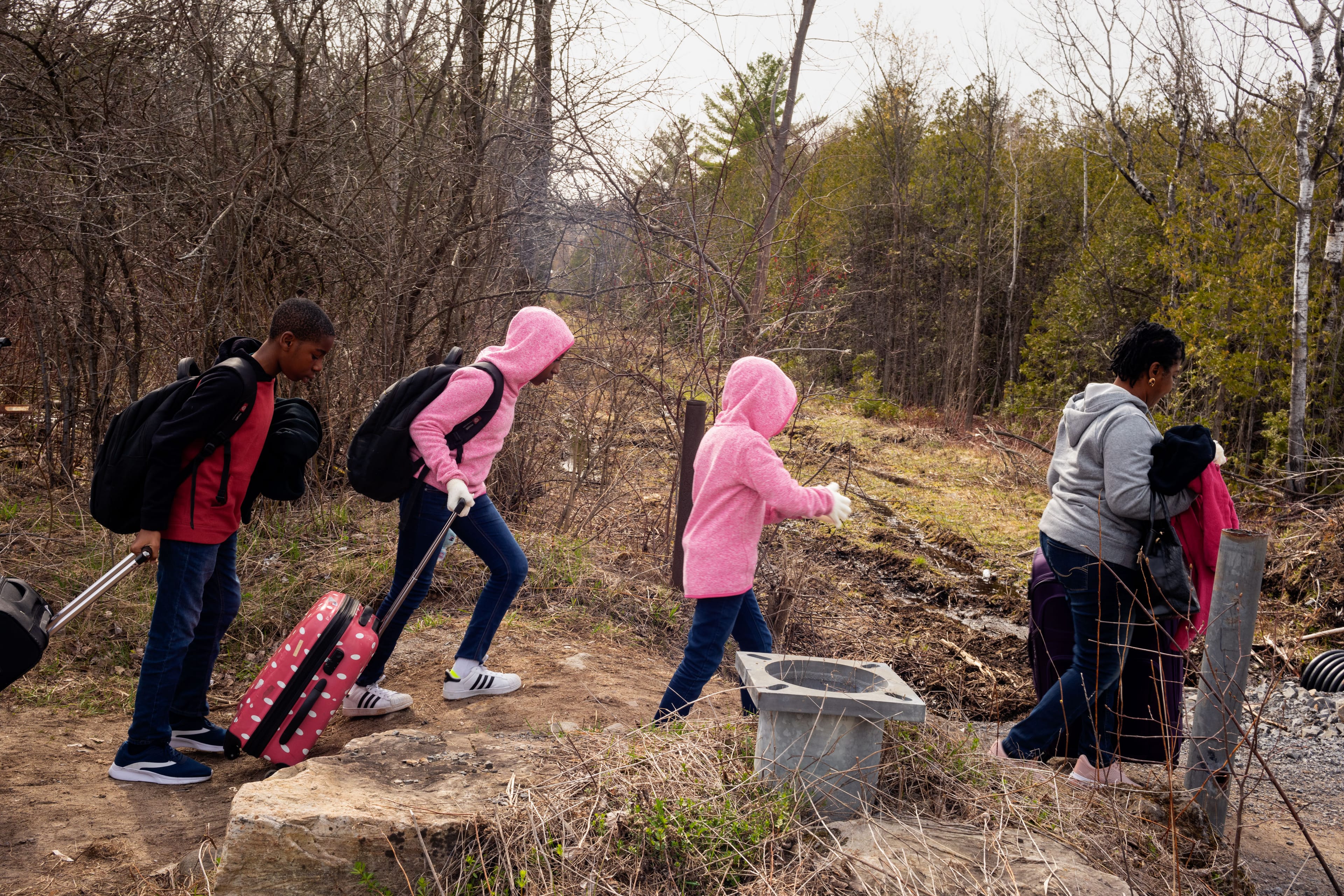 Kids in hoodies walking across a path with rolling suitcases.