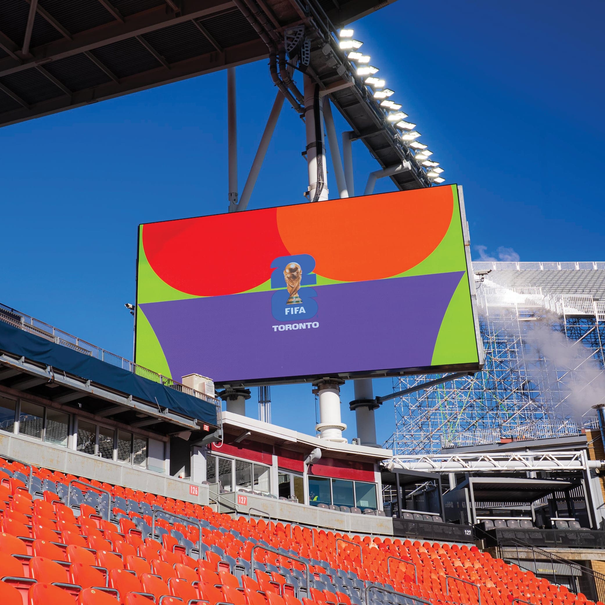 At the BMO Field, a large digital signage that displays the World Cup logo, saying "FIFA Toronto". Rows of empty red seats under it.