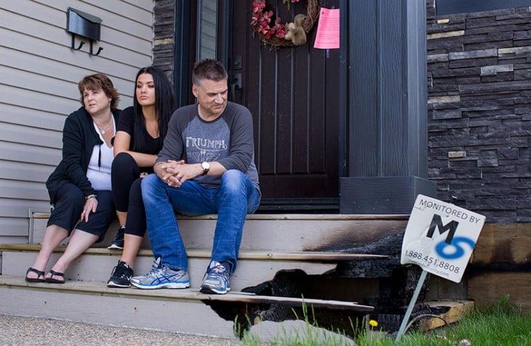 <p>Nolan and Kathy Palmquist and their 17-year-old daughter, Kelsey sit on the front steps of their home in the neighbourhood of Stonecreek in Fort McMurray on Thursday, June 02, 2016. Their 4-bedroom home on a corner lots had only damage to the vinyl siding and front steps, while all houses across from them burned to the ground. (Photograph by Chris Bolin)</p>
