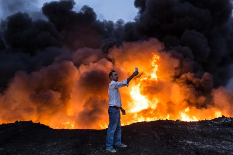 <p>October 19, 2016: A man takes a selfie in front of a fire from oil that has been set ablaze in the Qayyarah area, south of Mosul. (Basin AkgulAFP/Getty Images)</p>
