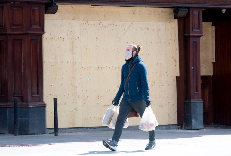 A man carries his groceries past a boarded up bar on Apr. 22, 2020 in Ottawa. (Adrian Wyld/CP)