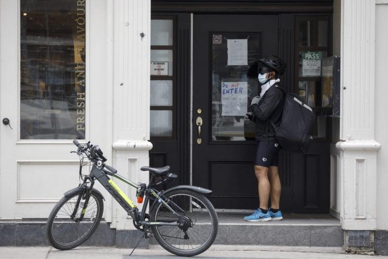 A food delivery courier wearing a protective mask waits for an order on Yonge St. in Toronto on March 25, 2020 (Cole Burston/Bloomberg/Getty Images)