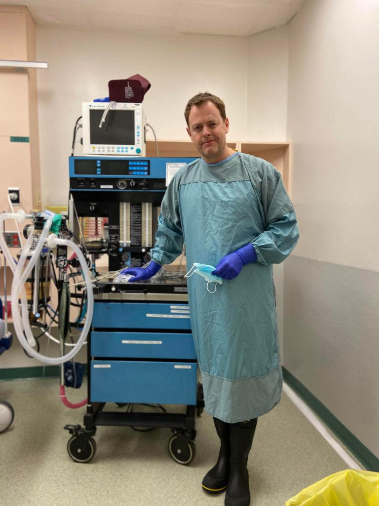 Dr Ivan Scrooby standing in front of an anesthetic machine that has a basic ventilator incorporated in the unit. (Photo courtesy of Dr. Scrooby)