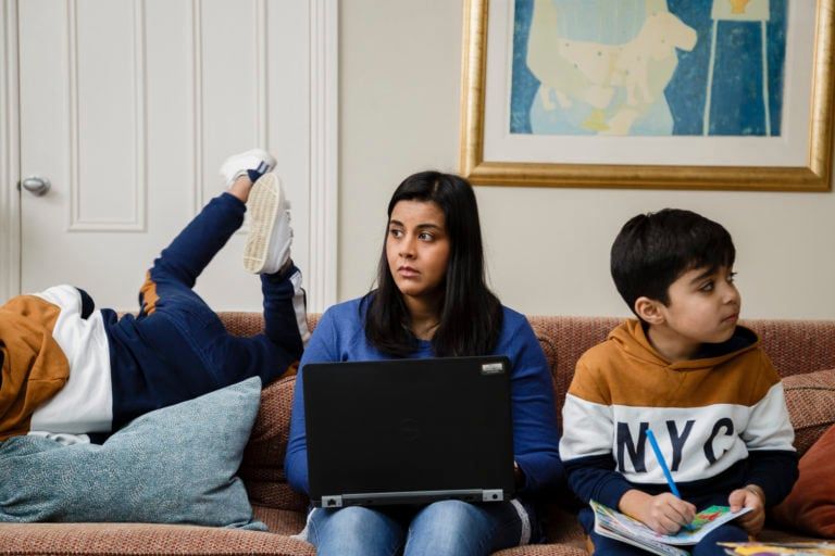 Woman sitting on couch with computer with two kids playing on either side