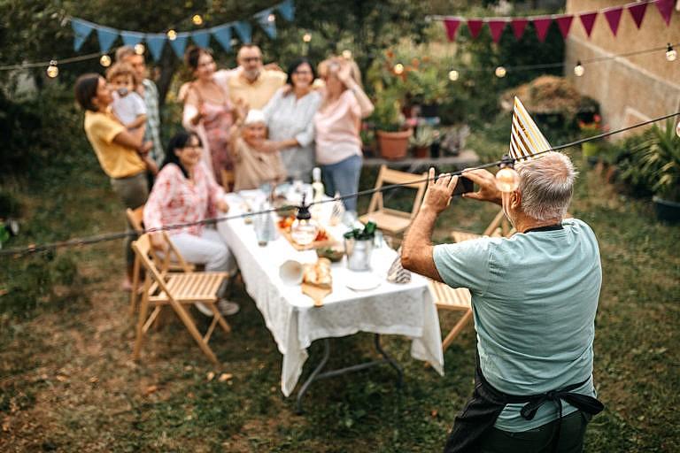 Old man capturing birthday party moments on a mobile phone in garden party