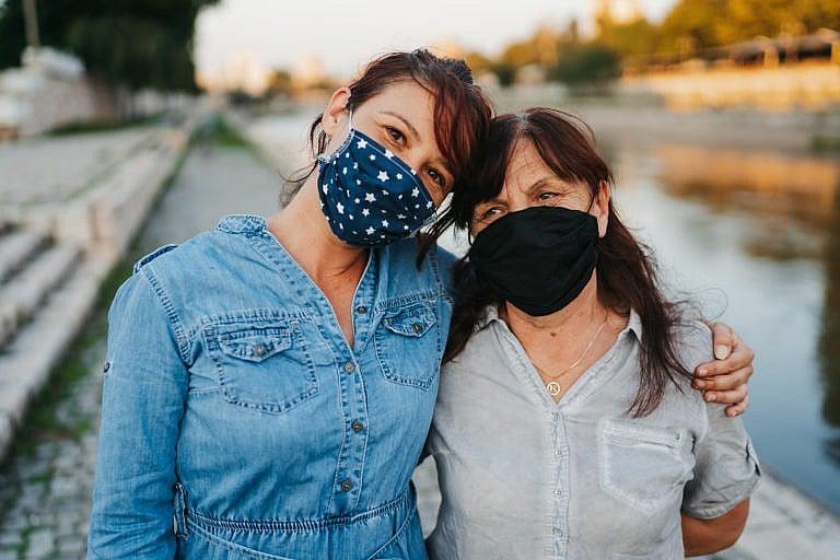 Portrait of senior woman and mid adult daughter with protective face mask standing and hugging on quayside in the city after long quarantine