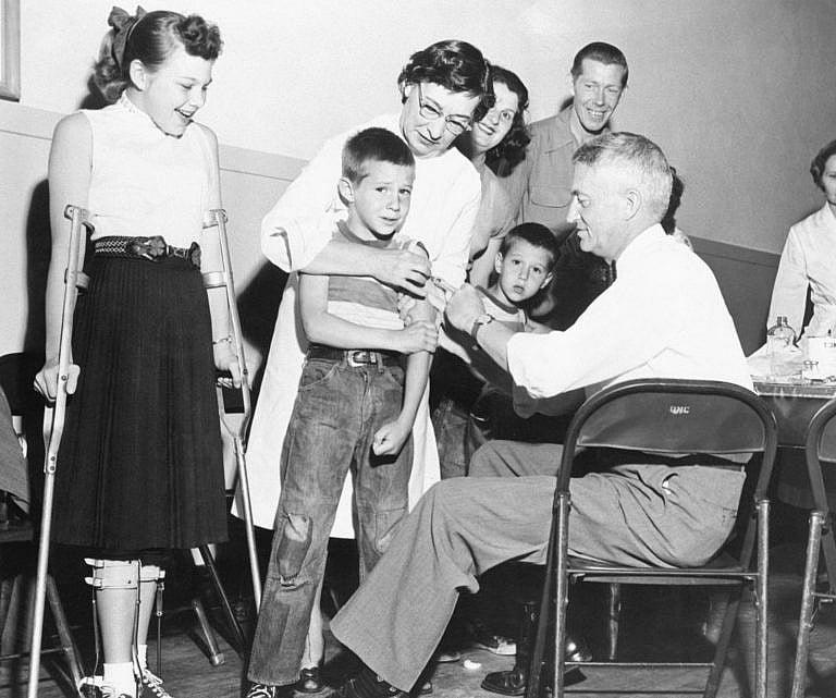 Dr. William S. Burgoyne gives a shot of the Salk anti-polio vaccine to Michael Urnezis, 6, while the boy's sister, Joanne, 12, a polio victim, looks on April 16. Smooth-working teams of doctors and nurses in San Diego completed the nation's first mass inoculation of school children with the vaccine after its approval by scientists and the government. Some 300,000 children were inoculated. (Bettmann/Getty Images)