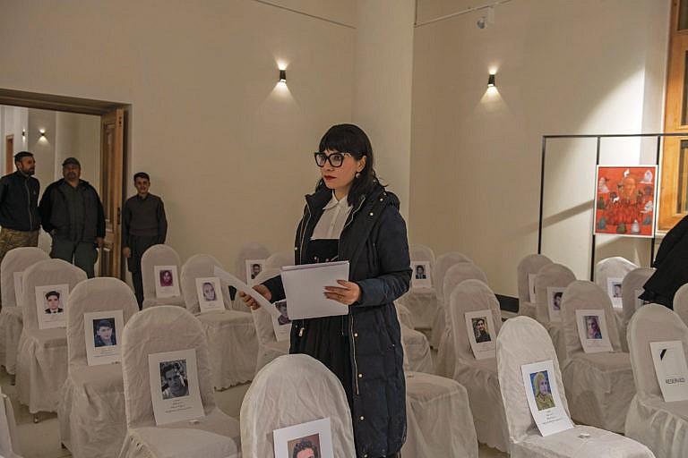 Akbar at her exhibit; each empty chair cradles the picture of a person killed by extremists (Kiana Hayeri/The New York Times)