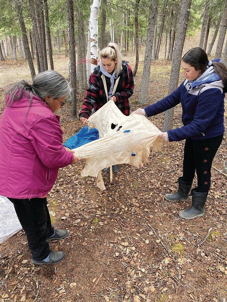 Students Kateri Lynn and Theresa Lynn work with Elder Madeline Judas to stretch the caribou hide after it has been soaked in a soup made from caribou brains. (Courtesy of Kyla LeSage/Dechinta Centre for Research and Learning)