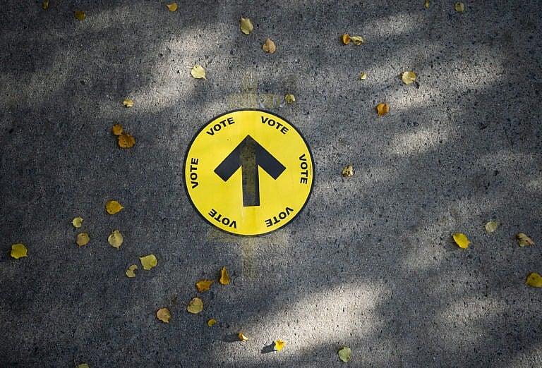 A sign directing voters to a polling station is taped to the sidewalk among autumn leaves, on election day of the 2019 federal election, in Ottawa, Monday, Oct. 21, 2019. (Justin Tang/CP)
