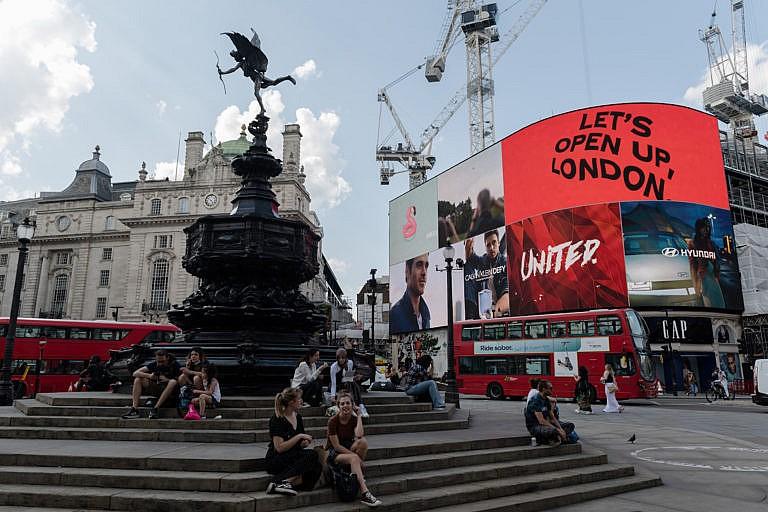 LONDON, UNITED KINGDOM - JULY 19: People sit in Piccadilly Circus as the light display reads 'Let's Open Up London' on the day of lifting of nearly all remaining coronavirus restrictions in London, United Kingdom on July 19, 2021. The removal of social and economic restrictions in England including social distancing, working from home, limits on gathering sizes and face mask mandate comes amid rapidly rising infection numbers driven by the Delta variant with UK daily Covid-19 cases exceeding 50,000 on two consecutive days last week. (Photo by Wiktor Szymanowicz/Anadolu Agency via Getty Images)