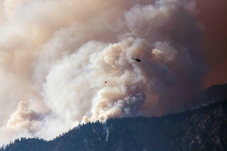 A helicopter prepares to make a water drop as smoke billows along the Fraser River Valley near Lytton, B.C., on July 2, 2021 (James MacDonald/Bloomberg/Getty Images)