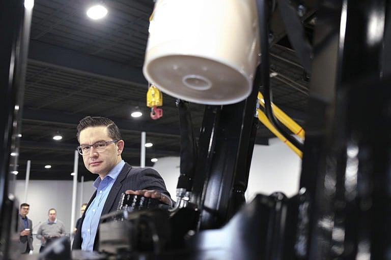 Poilievre glances at the camera briefly while getting a tour of machinery in Regina March 4, 2022. (Michael Bell/The Canadian Press)