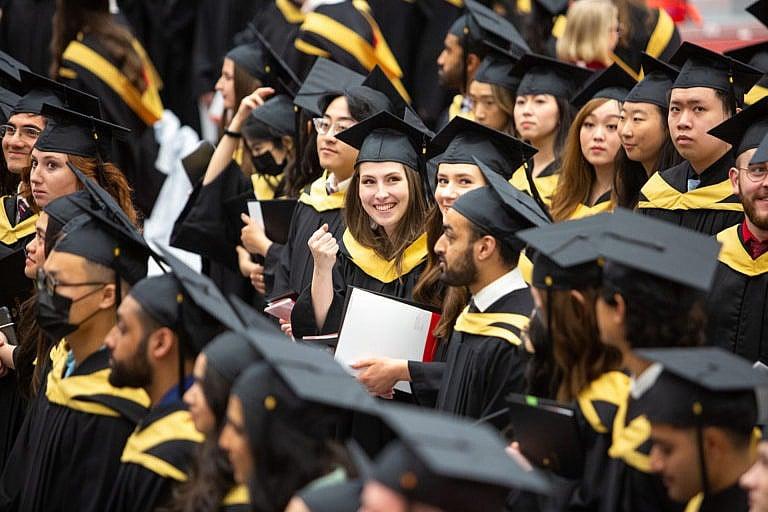 Students wearing black graduation caps and gowns standing in rows, smiling